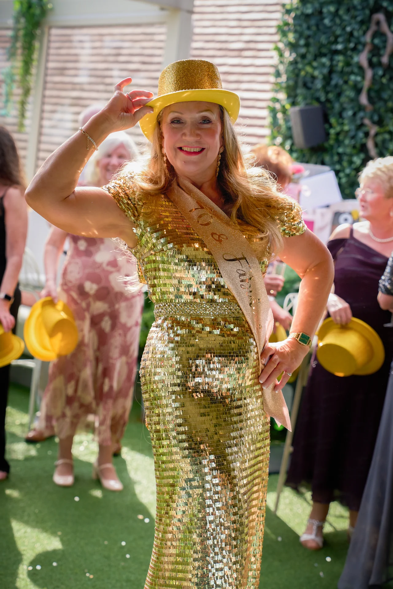 A guest in gold sequins and a yellow hat at a garden party